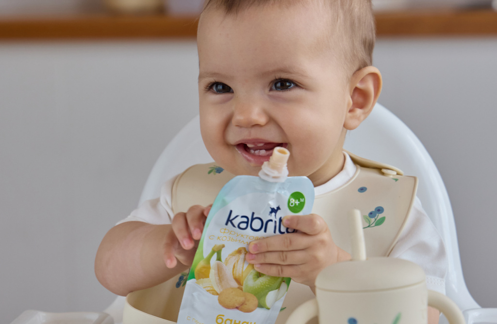 Малыш держит фруктовое пюре Kabrita